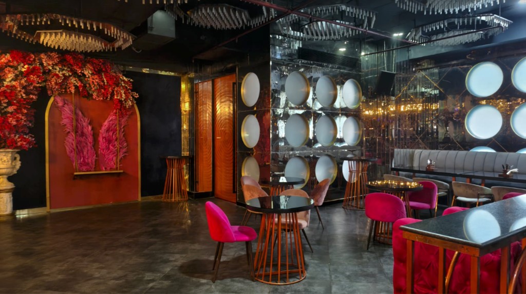 Floral lounge with pink velvet chairs, copper high tables, and a mirrored wall of circular lights