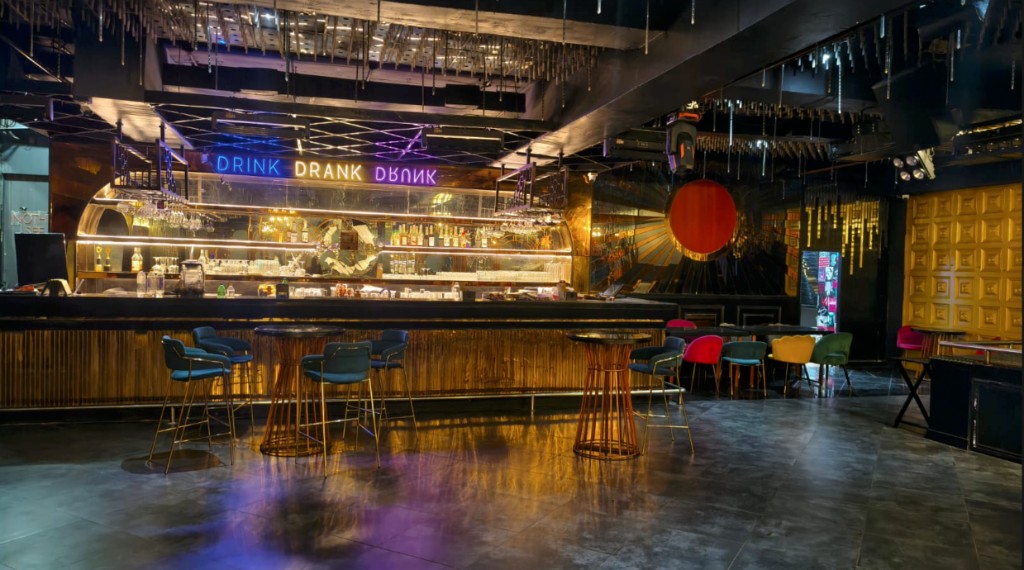 Bar counter at night with hanging lights, teal stools, and a gold door beyond