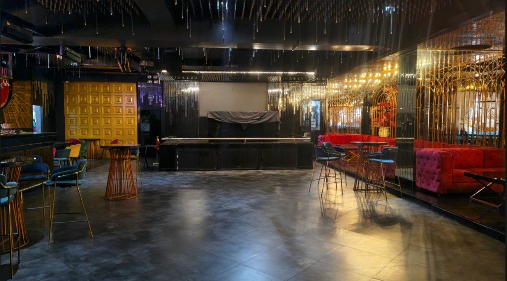 Open dance floor facing a black stage, with a gold door and red banquettes