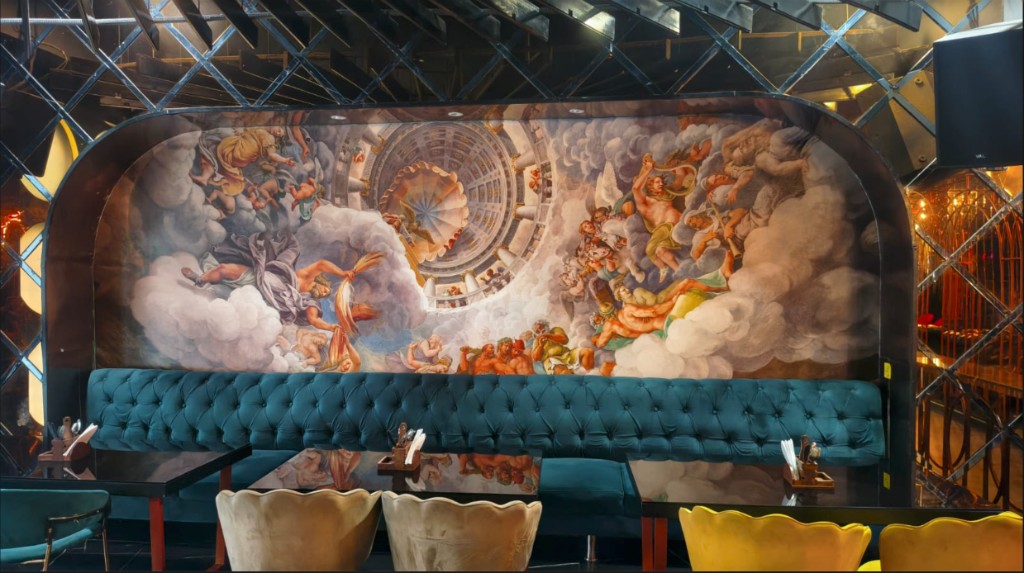 Teal tufted banquette beneath a large renaissance mural of figures in the clouds